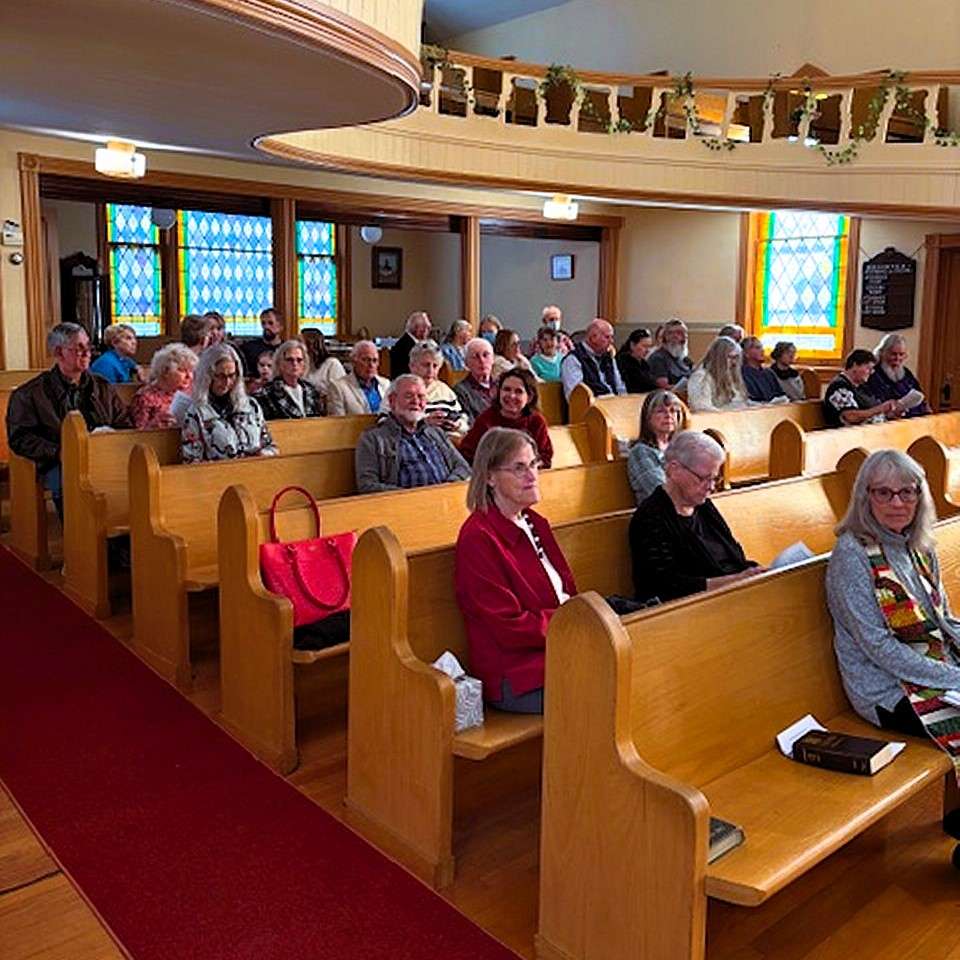 church sanctuary pews full of people of all ages and genders, curved balcony above their heads