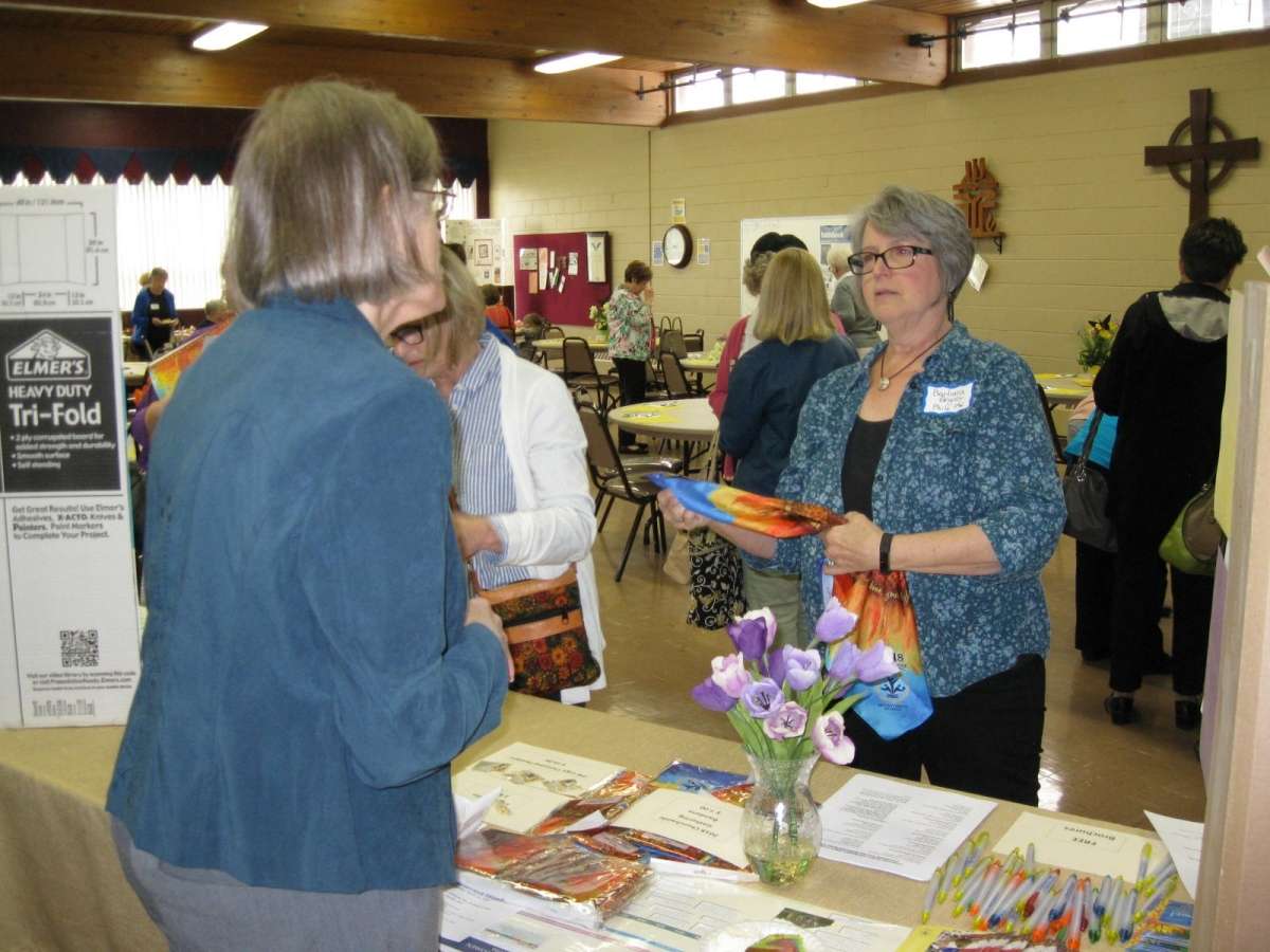 woman at indoor fair booth explains a topic to another interested woman